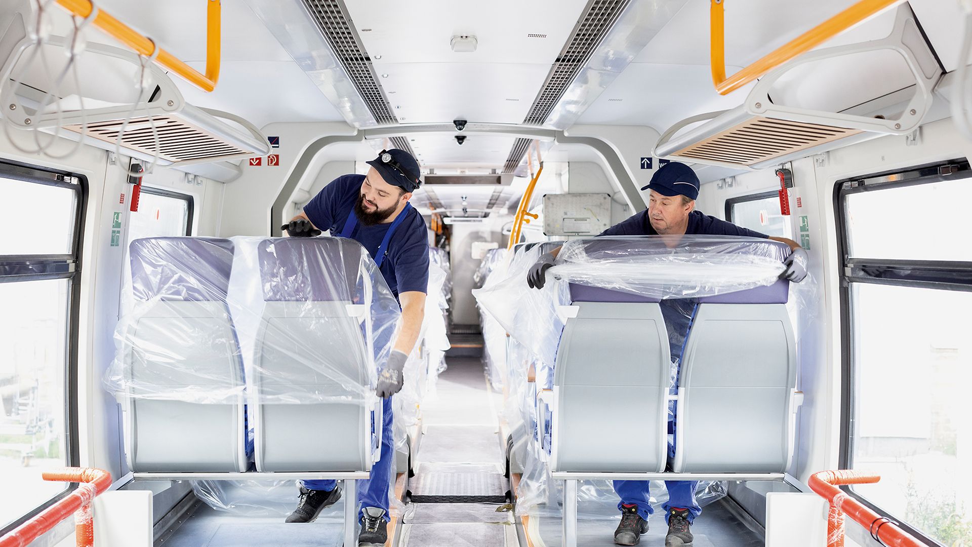 Zwei Alstom-Mitarbeiter überziehen Sitze im Zug mit Plastikfolie.