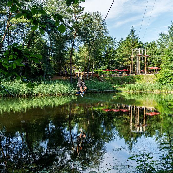 Ein Mensch ist an einer Zip-Line angeseilt und hängt im Wald über einem Gewässer.
