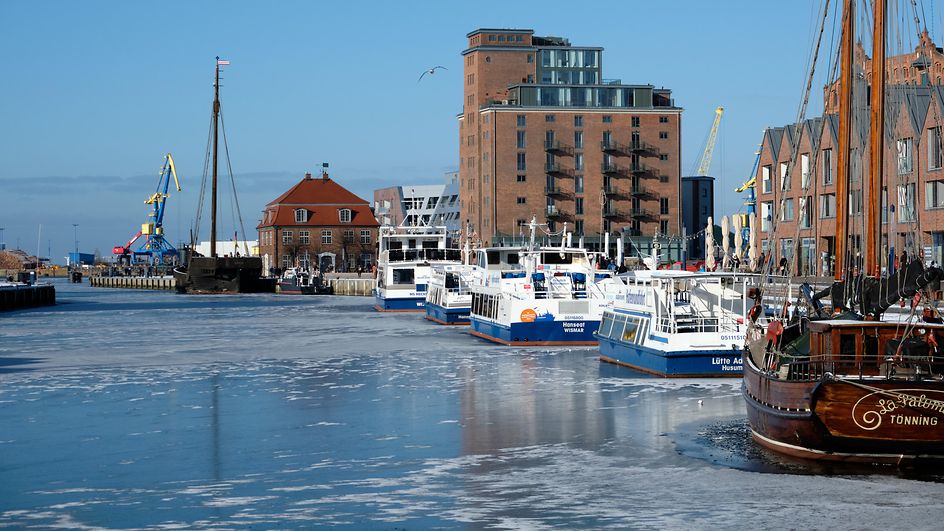 Blick auf den Hafen in Wismar. Zu sehen sind Speichergebäude und Boote im Wasser die zwischen Eisschollen liegen