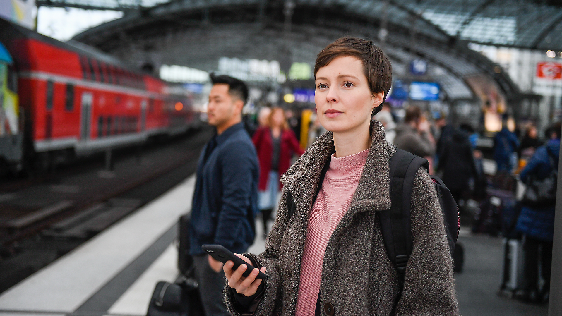 Frau hält ihr Smartphone und wartet am Bahngleis.