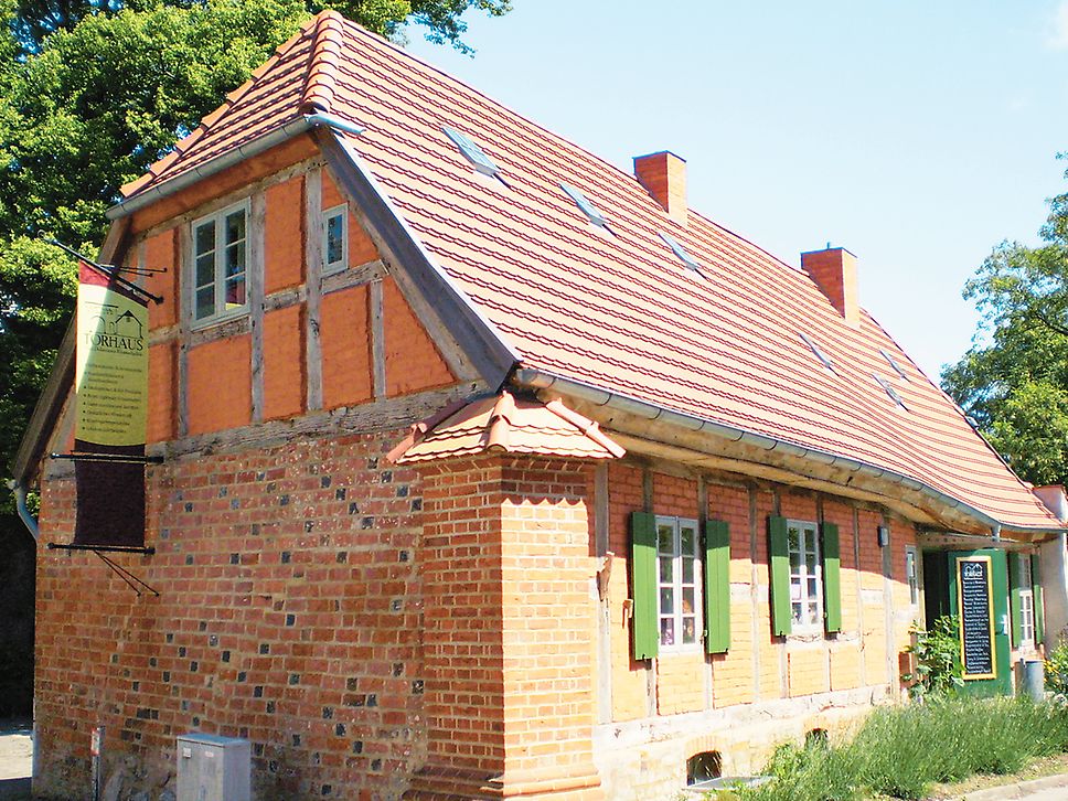 Ein anheimelndes Backsteinhaus mit Ziegeldach und grünen Fensterläden mit dem Schild „Torhaus“ 