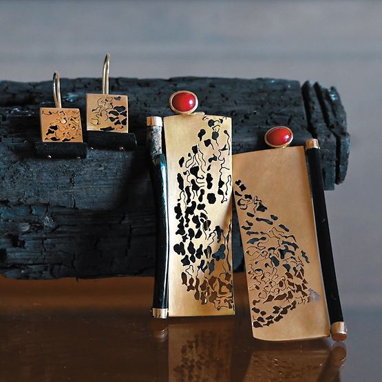Schmuck in Gold, Rot und Schwarz vor einem schwarzen Holzstück