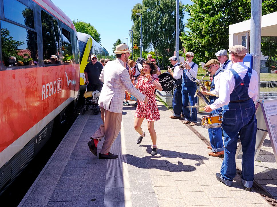 Paar tanzt neben einer spielenden Band am Regionalzug auf dem Bahnsteig in Graal-Müritz