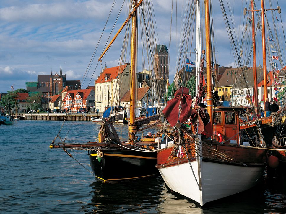 Segelboote ankern im Wasser, dahinter die Häuser und ein Kirchturm der Hansestadt Wismar