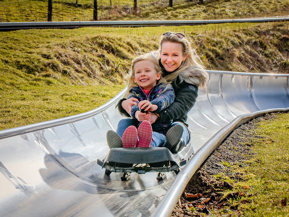 Eine Mutter fährt mit ihrer Tochter die Sommerrodelbahn in Burg Stargard herunter 
