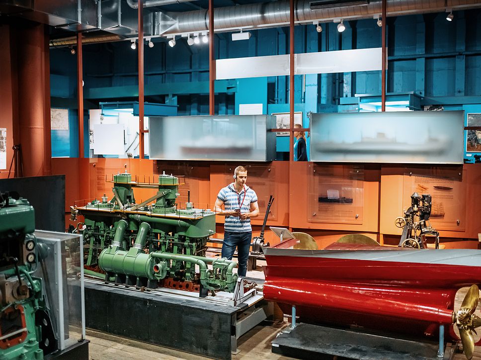 Ein junger Mann steht mit Kopfhörern und Audioguide im Schifffahrtsmuseum Rostock