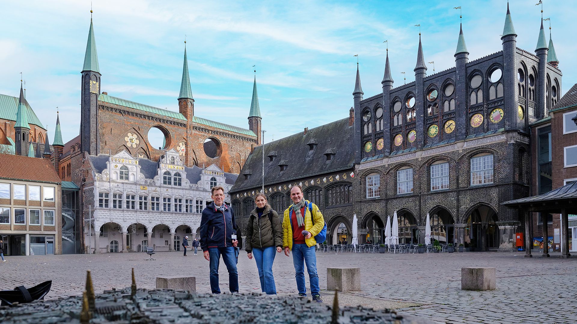 Podcast-Team mit Stadtführer Burkhard Stöß vor dem Lübecker Stadtmodell am Marktplatz, im Hintergrund das Rathaus