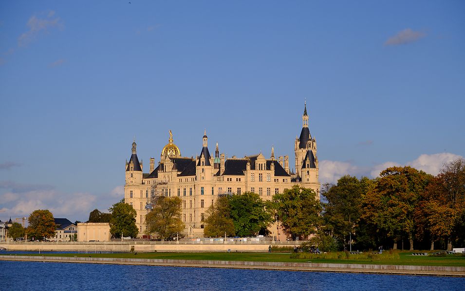 Das Schloss Schwerin mit seinen vielen Türmen, umrahmt von Bäumen, Rasen und Wasser 