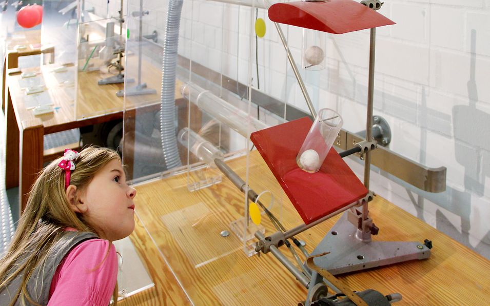 Ein Mädchen schaut interessiert in einen Schaukasten mit Röhren und Pingpongbällen im Otto-Lilienthal-Museum in Anklam