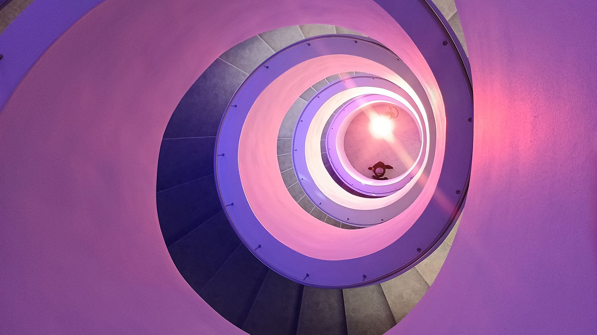 Blick von oben in das lila beleuchtete Treppenauge der modernen Wendeltreppe in der Philharmonie Stettin (Szczecin)