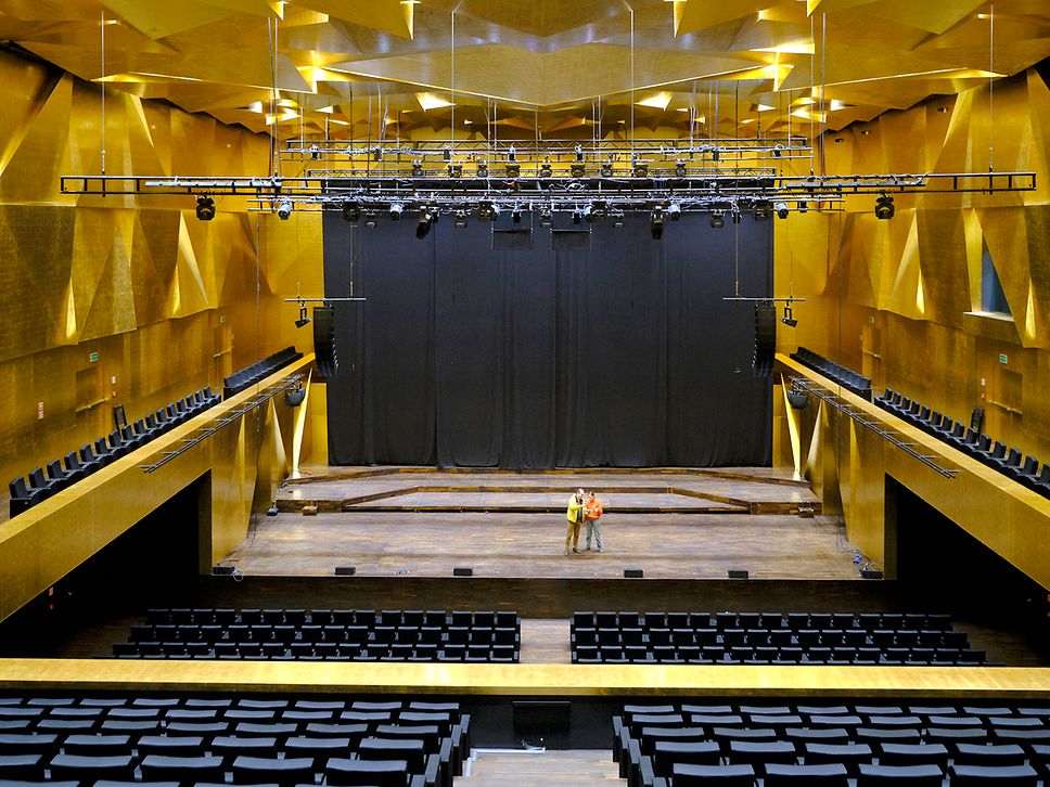 Der große Saal der Philharmonie Stettin mit goldenen Wand- und Deckenpaneelen sowie schwarzen Stuhlreihen 
