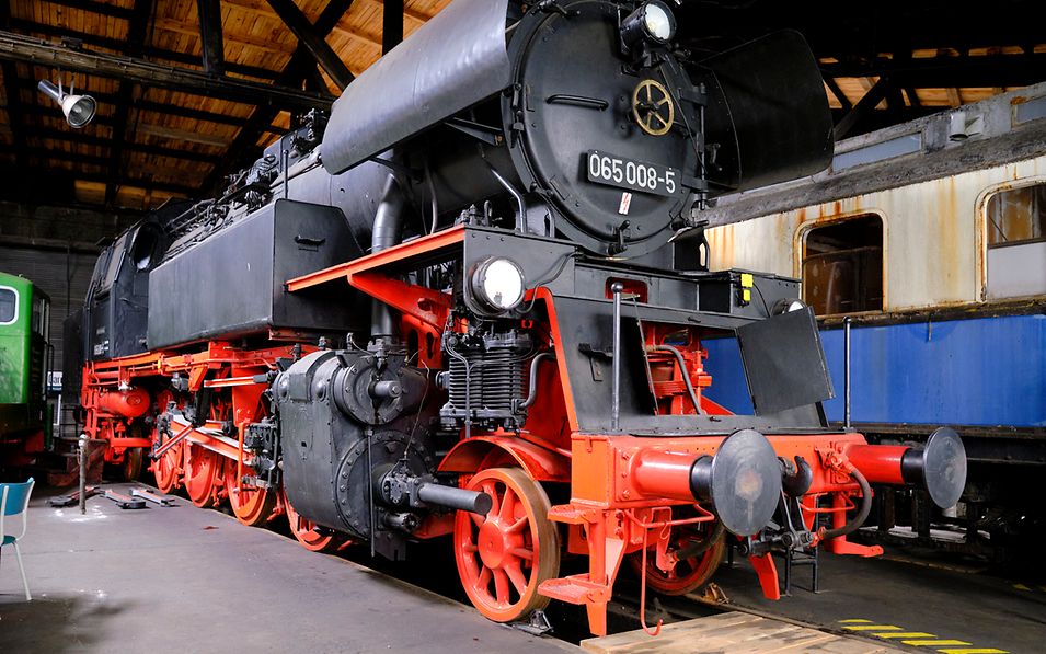 Eine historische Dampflok neben einem alten blau-weißen Waggon im Lokschuppen Pasewalk
