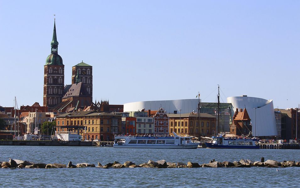 Blick über das Wasser auf die Stadt Stralsund mit der doppeltürmigen St. Nikolaikirche und dem Ozeaneum