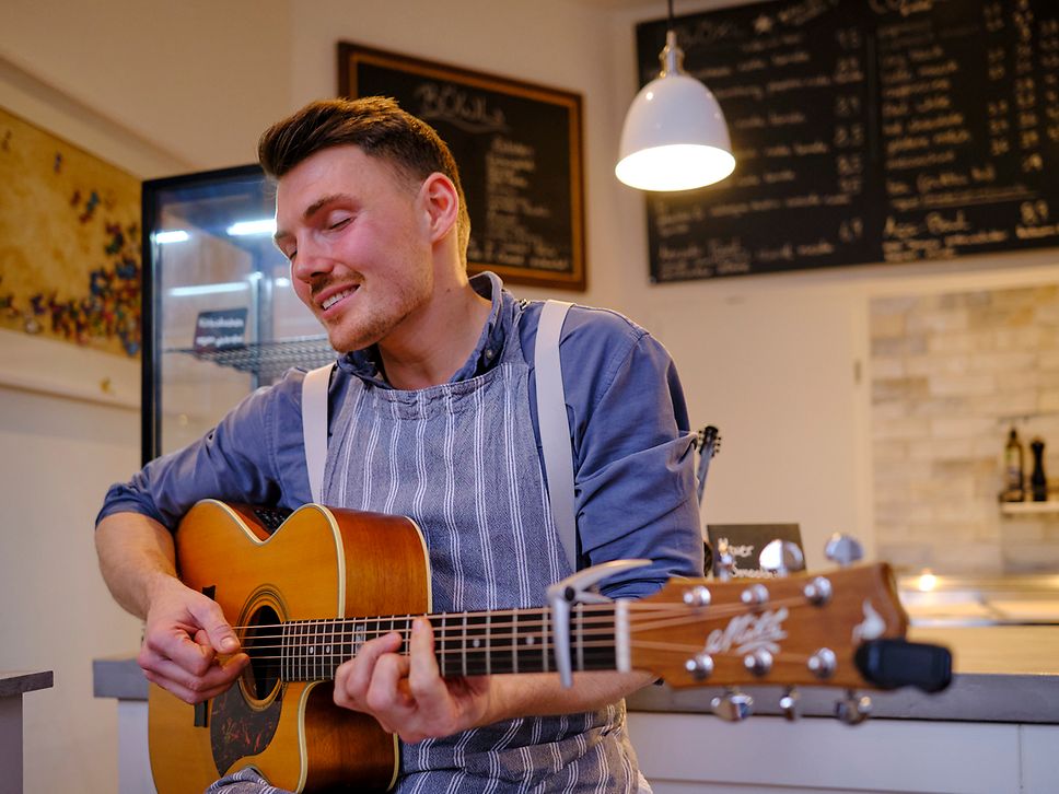 Der Musiker ÖXL spielt in seinem ÖXL Café in Wismar auf einer Gitarre 