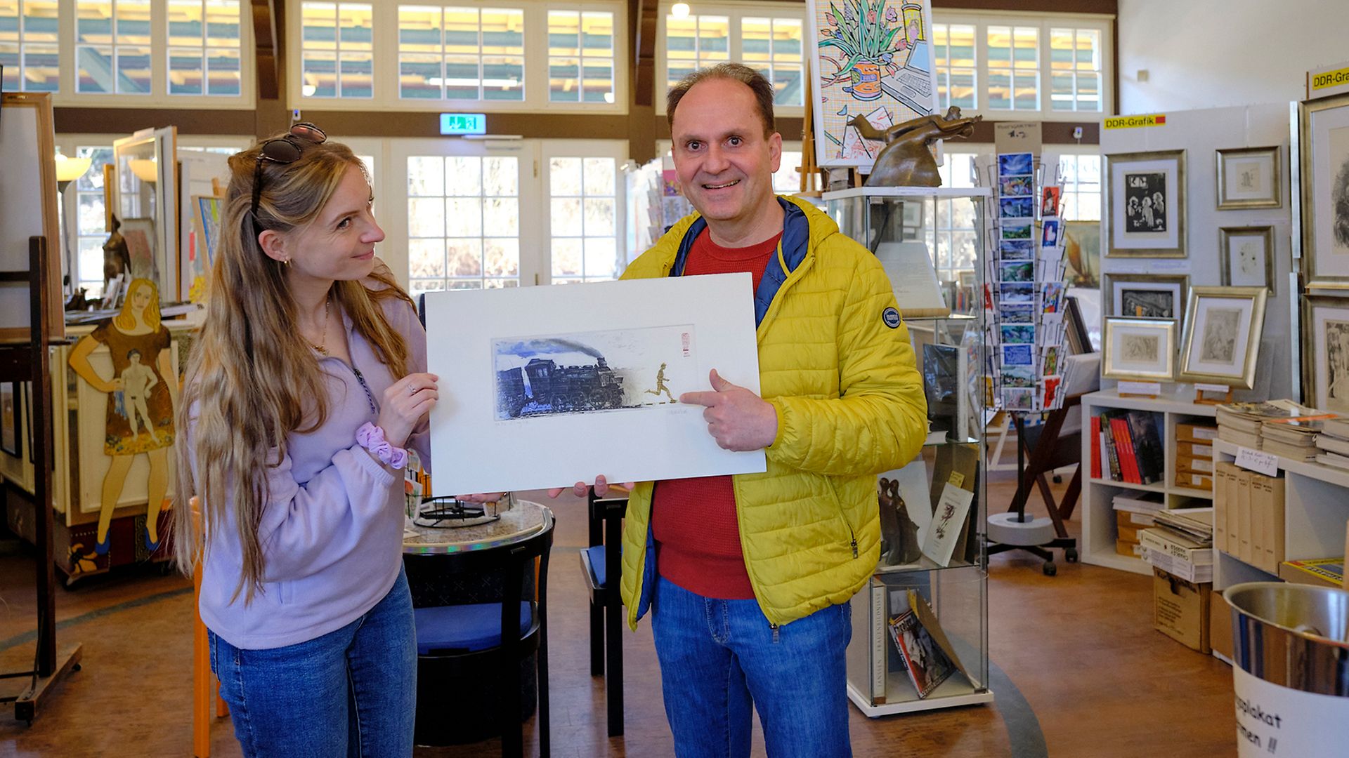 Maike und Ingo posieren in der Kunsthalle Ahlbeck mit dem Gemälde einer Dampflok.