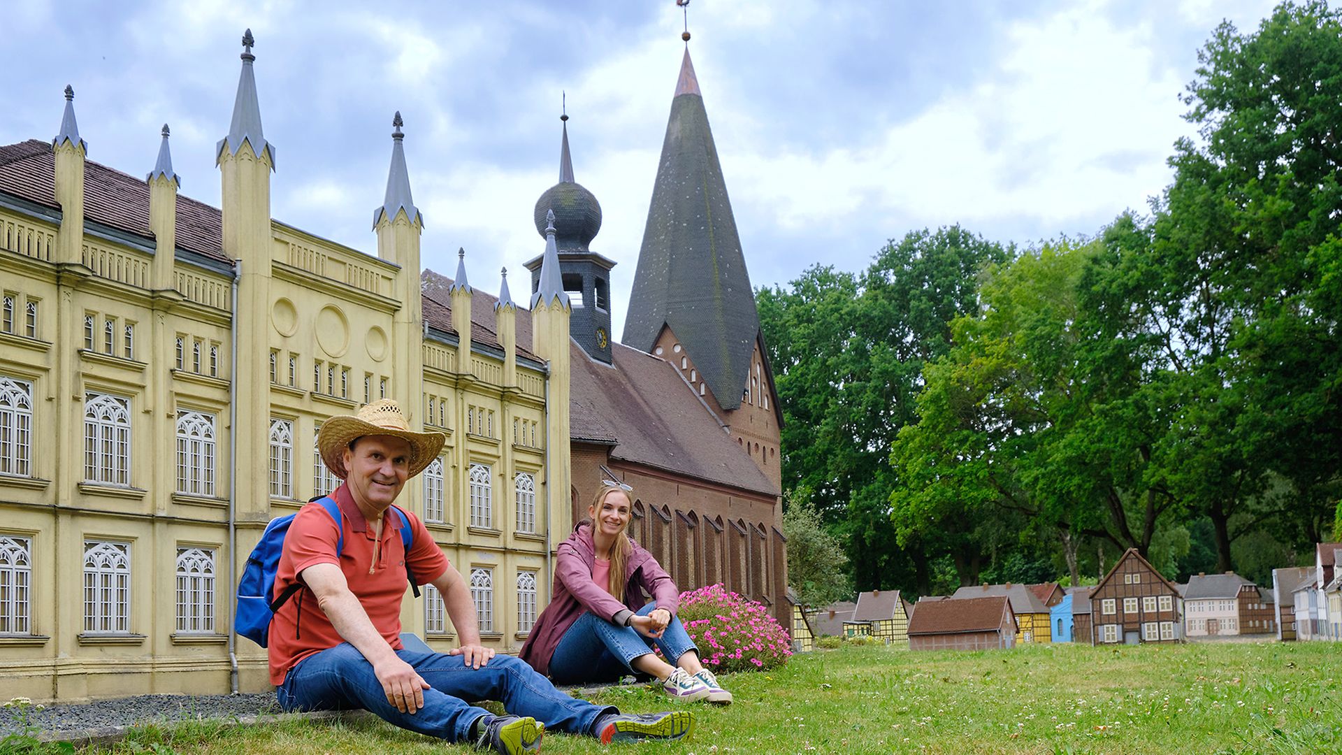 Ingo und Maike sitzen auf dem Rasen hinter den Nachbauten von Rathaus und Stiftskirche in der Miniaturstadt Bützow
