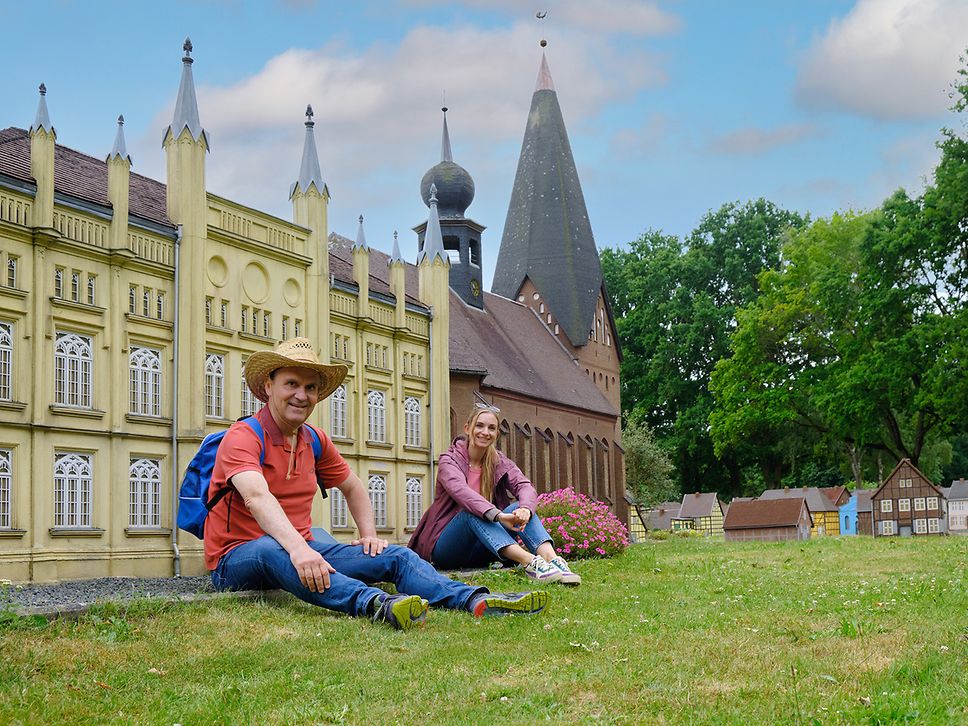 Zwei Personen vor dem Rathaus mit gelber Fassade im Tudor-Stil und der Stiftskirche mit markantem Turm in der Miniaturstadt.