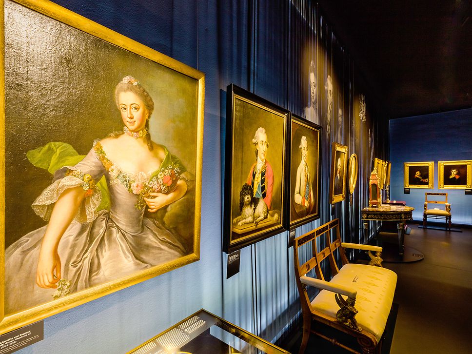 Historische Porträts in schwarzen und goldenen Rahmen an der dunkelblauen Wand des Kulturquartiers Neustrelitz 