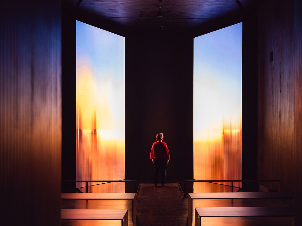 Eine Person steht vor einer Installation, bei der in zwei schwarzen Rahmen Impressionen in Licht und Farbe zu sehen sind 