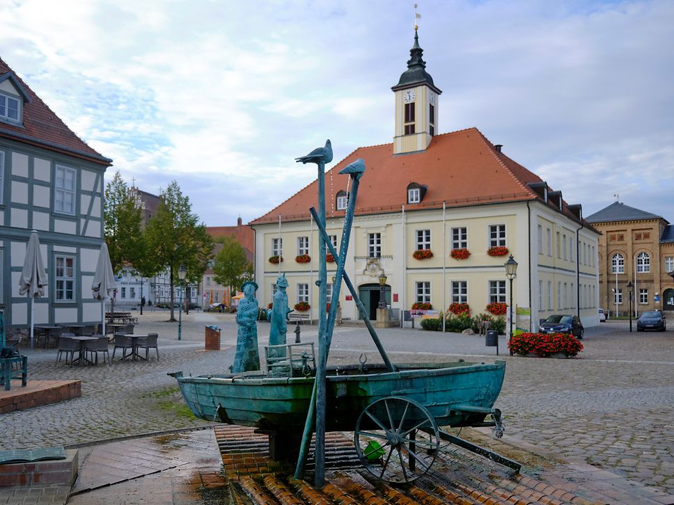 Der kopfsteingepflasterte Marktplatz in Angermünde mit Marktbrunnen im Vordergrund und dem Rathaus im Hintergrund. 